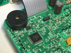 Zbliżenie na płytkę PCB z elementami elektronicznymi programatora zmywarki, widoczny czarny buzzer, mikrokontroler i różne podzespoły SMD.