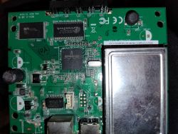 Zielona płytka PCB z modemu z układami scalonymi Broadcom i metalową osłoną ekranującą