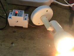 Electrical energy tester connected to a glowing light bulb on a wooden table.