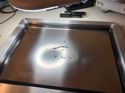 Metalloberfläche mit einer Reihe von Flüssigkeitstropfen unter einer Lampe auf einem Schreibtisch, mit Werkzeugen im Hintergrund.