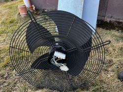 Wentylator ogrodowy z metalową osłoną i widocznymi przewodami elektrycznymi na trawie.