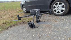Duży dron DJI Matrice 300 stojący na ziemi obok samochodu.