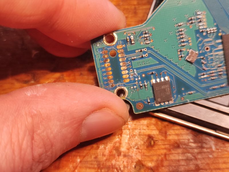 HDD Circuit Board with Moisture Damage Close-up of an HDD circuit board with visible moisture damage and fingers holding the board.