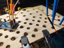 Close-up of a breadboard with an electronic module and wires attached on a wooden stand.