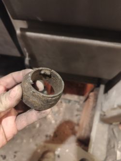 Zardzewiały metalowy pierścień trzymany w zabrudzonej dłoni przy podajniku opału