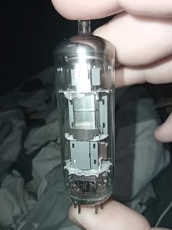 Osoba trzyma szklaną lampę elektronową z widocznymi elementami wewnętrznymi