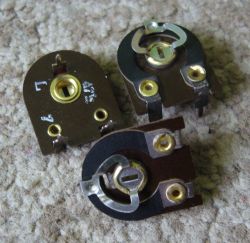 Three trimmer potentiometers with metal contacts on a gray textured surface