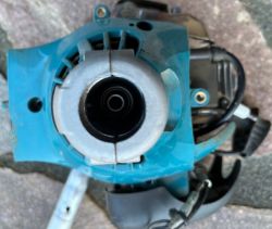 Zbliżenie na mechaniczną część kosy spalinowej z widocznym kołem zamachowym oraz obudową w kolorze niebieskim.