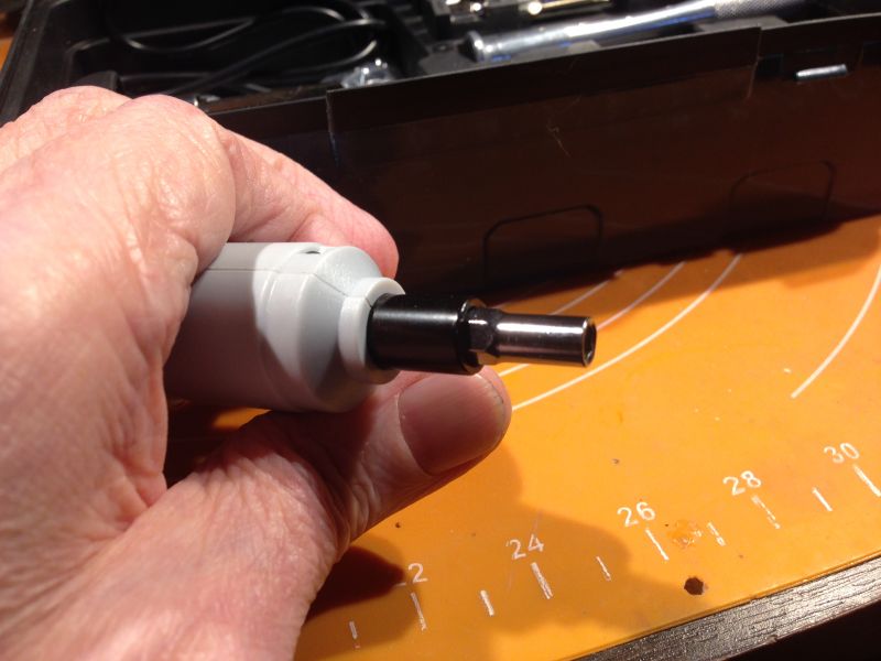 Ręka trzymająca elektryczny wkrętak z zestawem akcesoriów w tle.