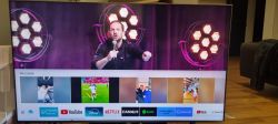 Telewizor Samsung wyświetlający program, z poziomymi paskami na jasnym tle w lewym górnym rogu.