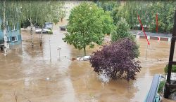 Widok zalanego terenu z dachami i drzewami wystającymi z wody.