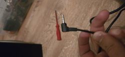 Dłoń trzyma kątowy wtyk mini jack 3,5 mm na czarnym kablu nad drewnianą podłogą