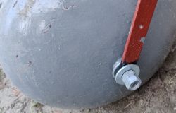 Zbliżenie na metalowy walec ogrodowy z uchwytem zamocowanym śrubą i nakrętką.