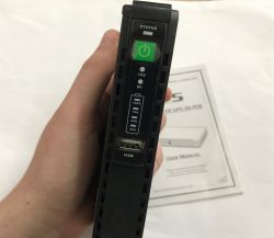 Hand holding a black mini UPS with green power button, 12V/9V LEDs, battery indicator, and USB port