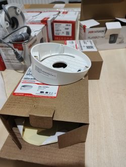 Biała puszka montażowa Hikvision na pudełkach z akcesoriami i kamerami na stole