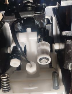 Zbliżenie na wnętrze urządzenia: biały zawór plastikowy, czarne przewody i metalowa sprężyna
