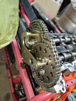 Zbliżenie na mechanizm rozrządu z łańcuchem i trybem na stole warsztatowym.