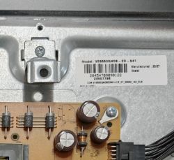Close-up of a metal chassis with a model label and part of a PCB with capacitors and a wire connector