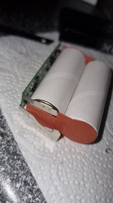 Otwarty pakiet baterii z dwiema białymi ogniwami cylindrycznymi i płytką PCB na ręczniku papierowym