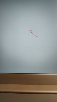 Jasna plamka na środku ekranu laptopa, zaznaczona czerwoną strzałką.