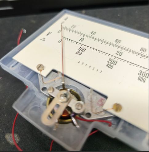 Zbliżenie mechanizmu wskaźnika analogowego z czerwoną wskazówką i skalą pomiarową