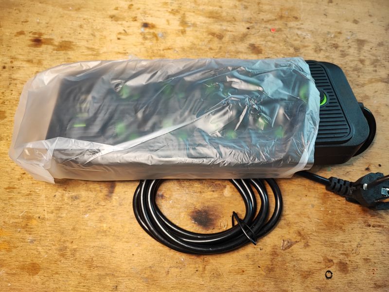 Przedłużacz z wieloma gniazdami i portami USB zapakowany w przezroczystą folię, leżący na drewnianym blacie.