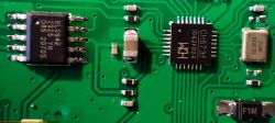 Close-up of a circuit board with visible SMD components, including integrated circuits and a quartz crystal resonator.
