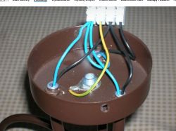 Mocowanie instalacji elektrycznej w brązowej puszce z odsłoniętymi kolorowymi przewodami.
