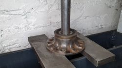 Hub with bearing and vertical shaft mounted on a steel frame, against a white brick wall