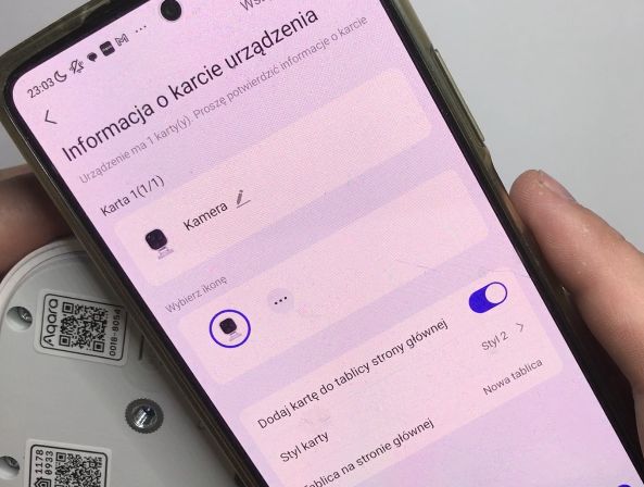 Telefon z ekranem konfiguracji kamery, trzymany nad urządzeniem z kodem QR