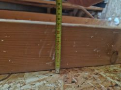 Miarka mierząca deskę grubości około 12 cm na tle płyty OSB