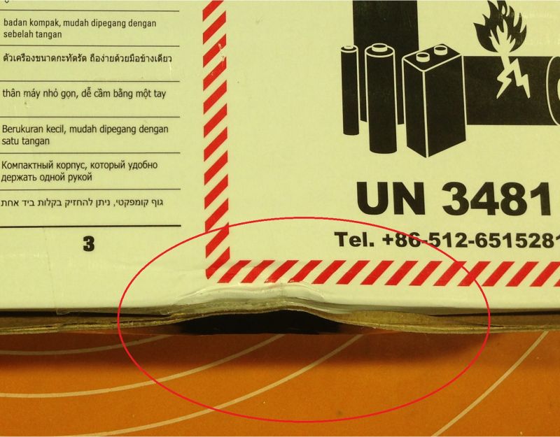 Kartonowe pudełko z wgnieceniem i symbolem baterii przy ostrzeżeniu o niebezpieczeństwie.