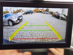 Widok z kamery cofania samochodu pokazujący zaparkowany samochód po lewej stronie.