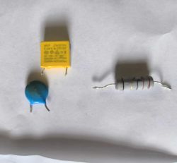 Trzy elementy elektroniczne: żółty kondensator, niebieski warystor, szary rezystor z kolorowymi paskami.