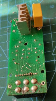 Spód zielonej płytki PCB z radiatorem i żółtym kondensatorem na macie z siatką