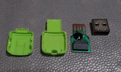Rozebrany czytnik kart USB z zieloną obudową, z widocznymi wszystkimi częściami: dwie połówki obudowy, płytka drukowana i metalowa końcówka USB.