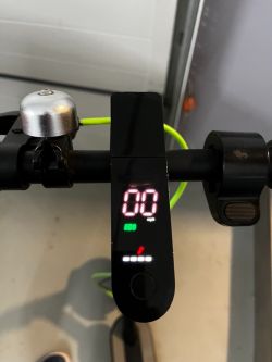 Hulajnoga elektryczna z widocznym wyświetlaczem, czerwonym kluczykiem i dzwonkiem.