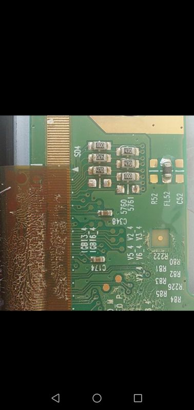 Close-up of a green PCB with SMD components and printed labels, next to a flex ribbon