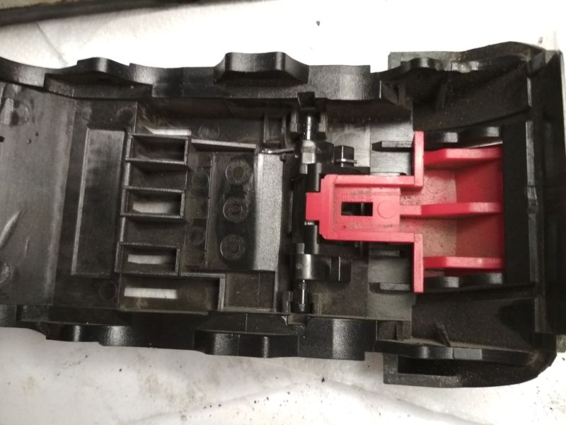 Wnętrze obudowy akumulatora z widocznym mechanizmem zaczepu, głównie w kolorze czarnym i czerwonym.
