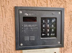 Stary domofon na ścianie budynku z klawiaturą numeryczną i wyświetlaczem.