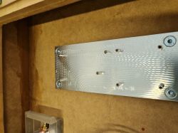 Wnętrze subwoofera z aluminiową płytą montażową i otworami na śruby.