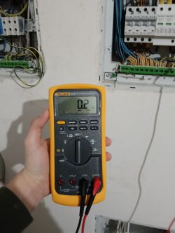 Multimetr pokazujący wynik pomiaru obok rozdzielnicy elektrycznej