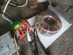 Zbliżenie na chiński moduł elektroniczny z podłączonym transformatorem toroidalnym i przewodami na betonowej podłodze.