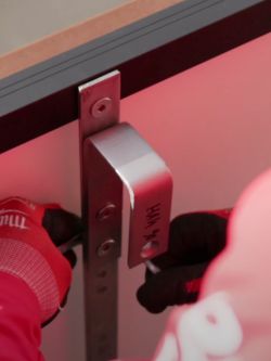 Osoba mocująca metalowy płaskownik na balustradzie za pomocą narzędzia.