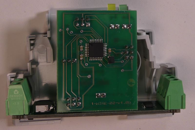 Płytka drukowana z elektroniką zamontowana w obudowie do szyny DIN, widoczne złącza śrubowe i układ scalony.