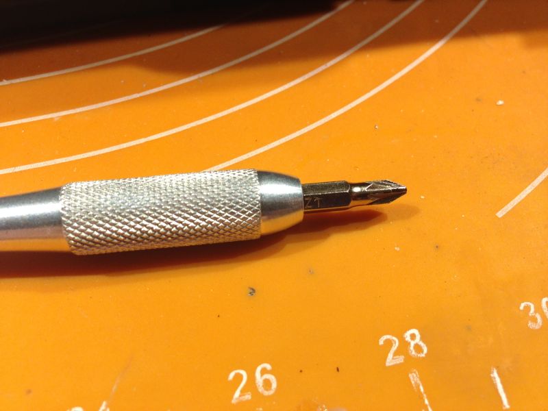 Metalowy uchwyt wkrętaka z założonym grotem krzyżakowym na pomarańczowej macie.