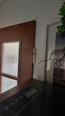 Brązowe drzwi z przeszkleniem i widocznym zawiasem, obok szara metalowa futryna z szybą