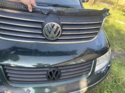 Osoba trzymająca grill samochodowy z emblem logiem Volkswagena na ciemnozielonym Passacie.