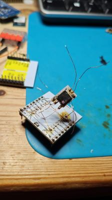 Small circuit board with thin wires and a scorched component on a blue work mat