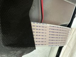 White ribbon cable with printed specs and a red-and-black wire next to a metal housing